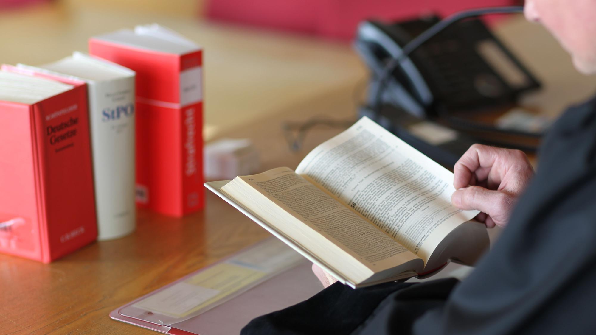 Ein Richter sitzt am Tisch und blättert in Gesetzbüchern.