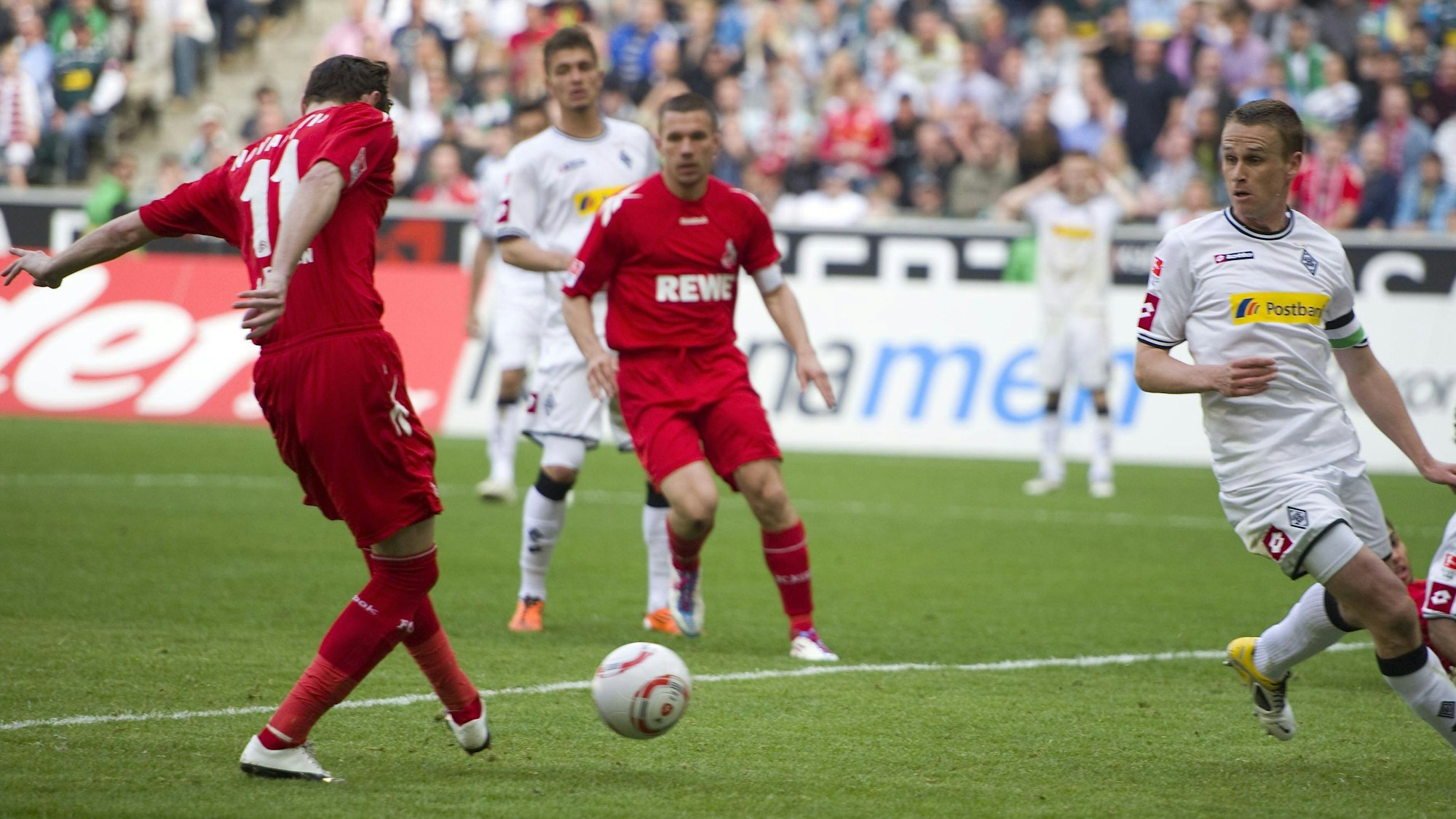 Der in rot gekleidete Stürmer des 1. FC Köln lässt zwei Gegenspieler aussteigen und erzielt ein Tor. Einer seiner Mitspieler schaut zu.