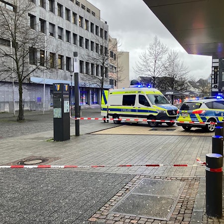 Zwei Polizeiautos stehen vor einem Bankgeschäft. Davor ist ein Tatport mit Flatterband abgesperrt worden.
