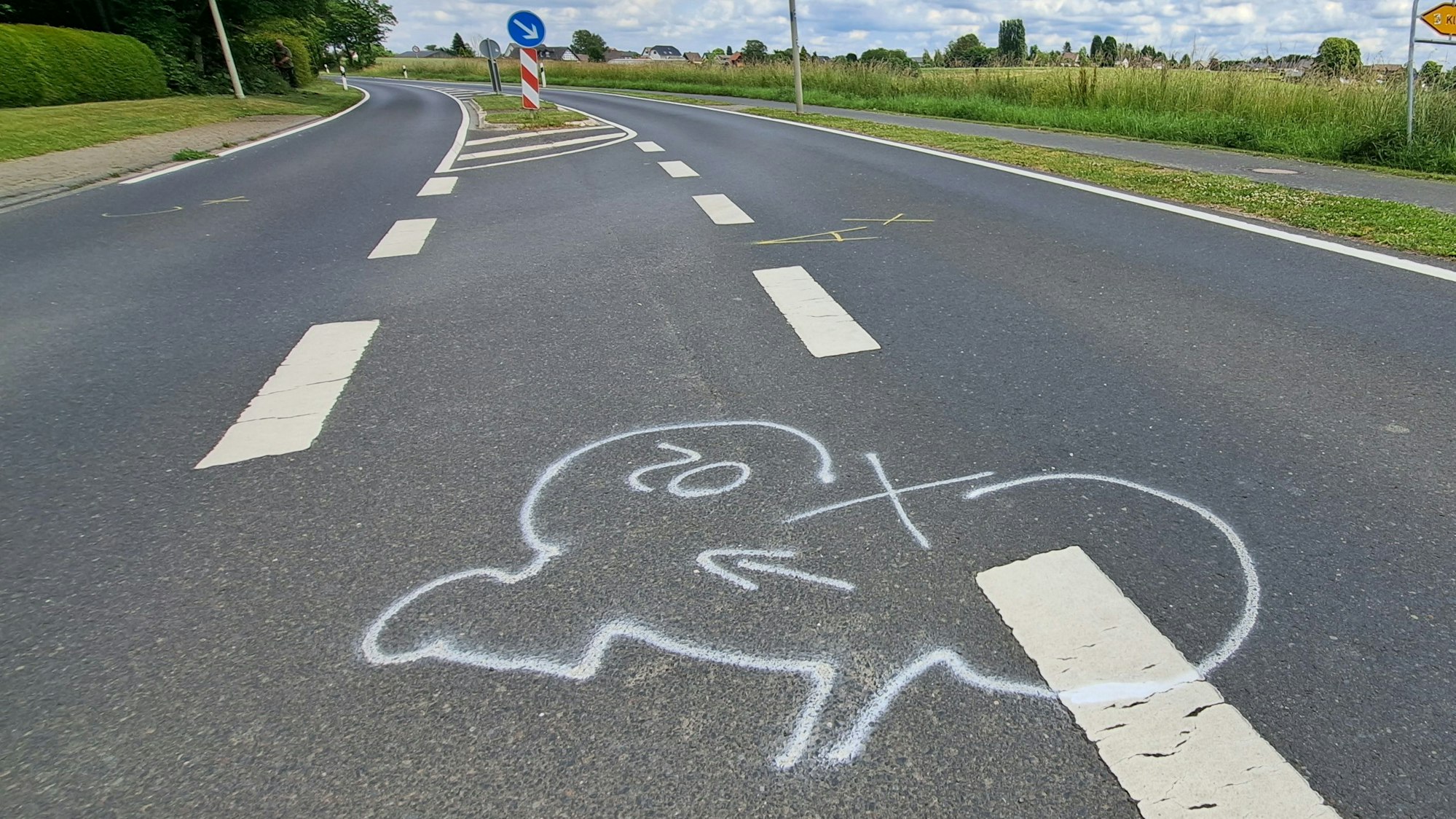 Auf einer Straße außerorts ist auf dem Boden mit weißer Kreide der Umriss eines Fahrrads eingezeichnet.