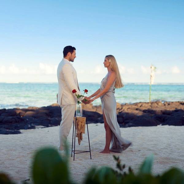 Larissa und Sebastian stehen gemeinsam an einem Strand und halten Händchen.