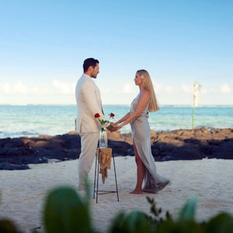 Larissa und Sebastian stehen gemeinsam an einem Strand und halten Händchen.