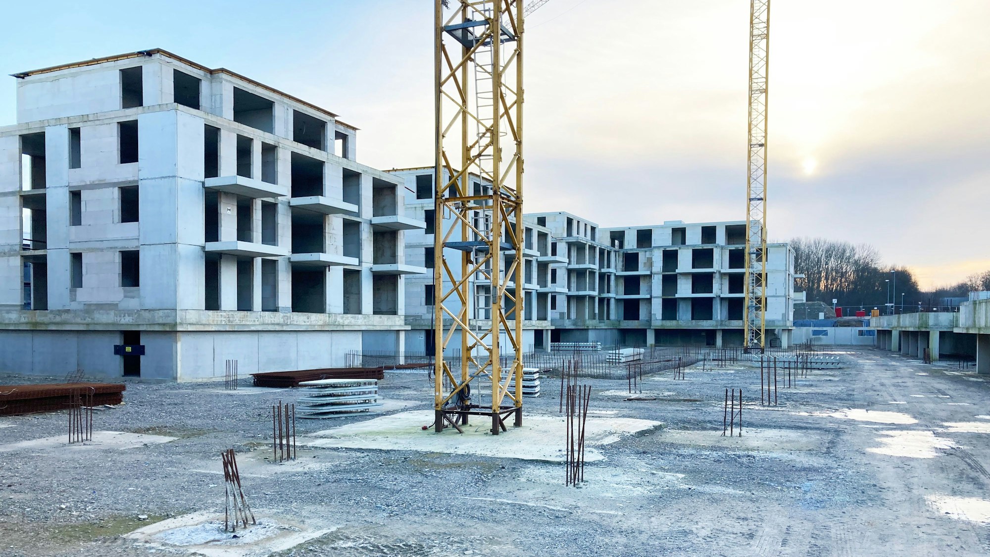 Vor großen Rohbauten stehen zwei gelbe Baukräne.
