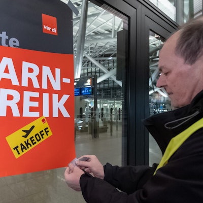 Ein Verdi-Vertreter befestigt ein Plakat mit der Aufschrift «Warnstreik» an einem Terminal im Hamburger Flughafen mit Klebestreifen. Im Hintergrund ist ein leeres Flughafenterminal zu sehen.