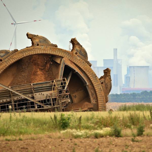 Ein Braunkohlebagger baggert im Tagebau Garzweiler, im Hintergrund steht ein Kraftwerk hinter Windrädern. (Archivbild)