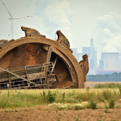 Ein Braunkohlebagger baggert im Tagebau Garzweiler, im Hintergrund steht ein Kraftwerk hinter Windrädern. (Archivbild)