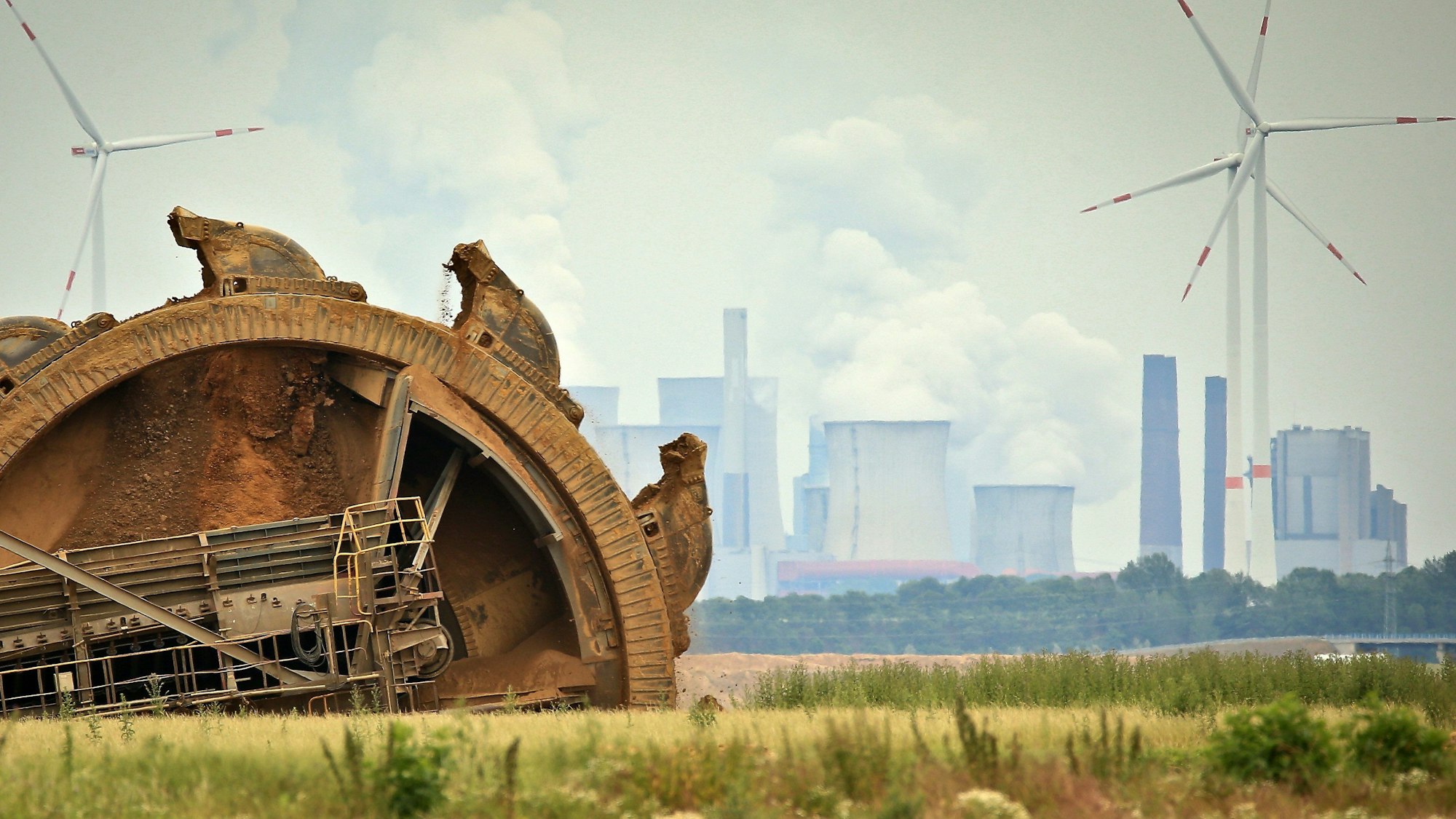 Ein Braunkohlebagger baggert im Tagebau Garzweiler, im Hintergrund steht ein Kraftwerk hinter Windrädern. (Archivbild)