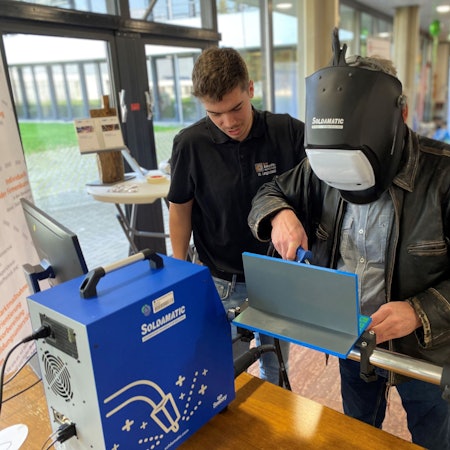 Ein älterer Mann arbeitet am Schweißgerät, ein jüngerer instruiert ihn.