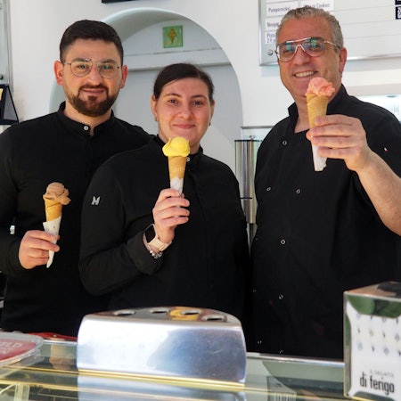 Zwei Männer und eine Frau halten Eishörnchen mit verschiedenfarbigen Eiskugeln in die Höhe.