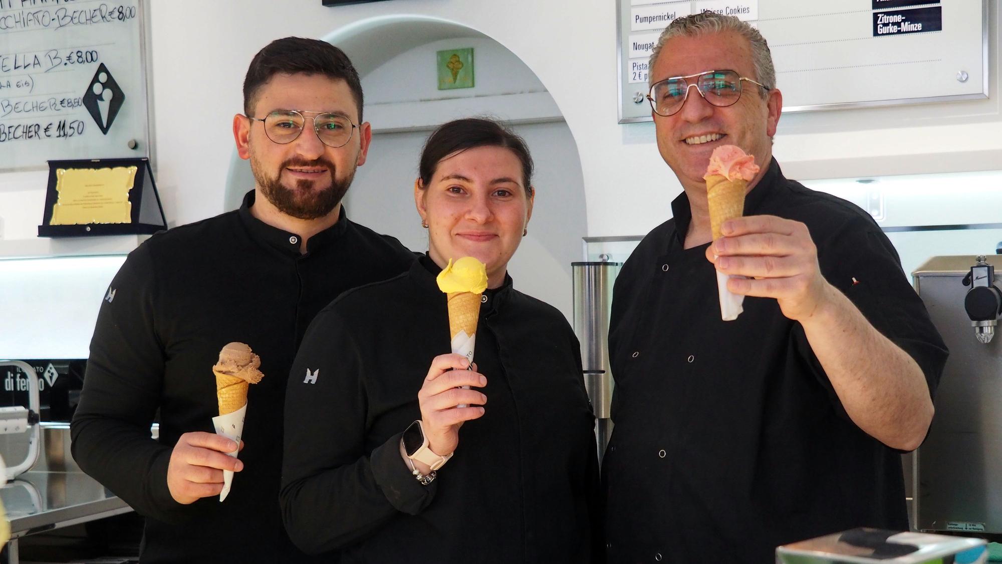 Zwei Männer und eine Frau halten Eishörnchen mit verschiedenfarbigen Eiskugeln in die Höhe.