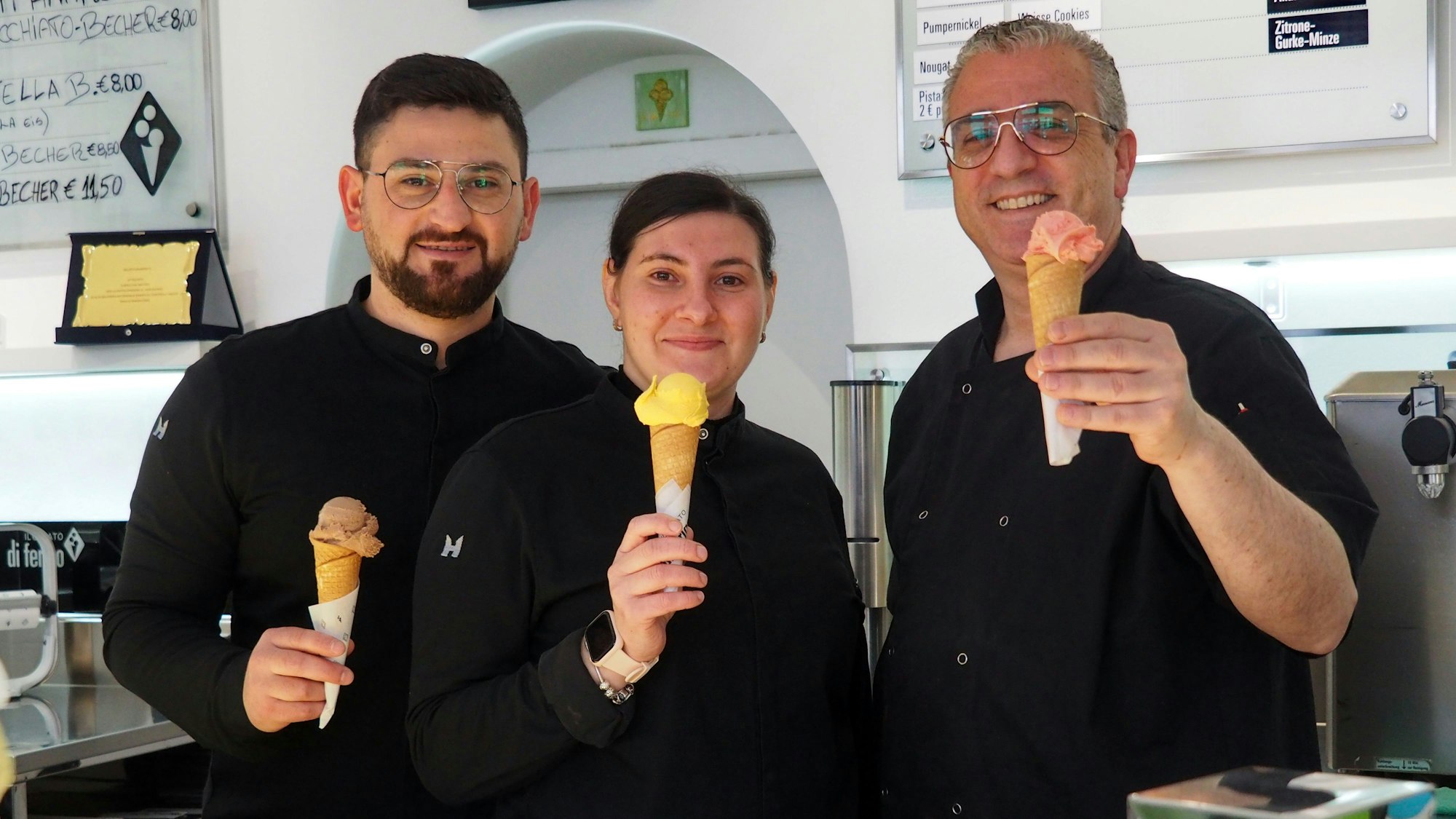 Zwei Männer und eine Frau halten Eishörnchen mit verschiedenfarbigen Eiskugeln in die Höhe.