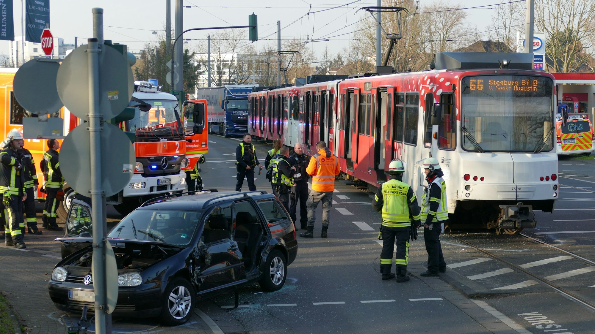 Feuerwehrleute stehen um eine Straßenbahn und ein zerstörtes Auto herum.