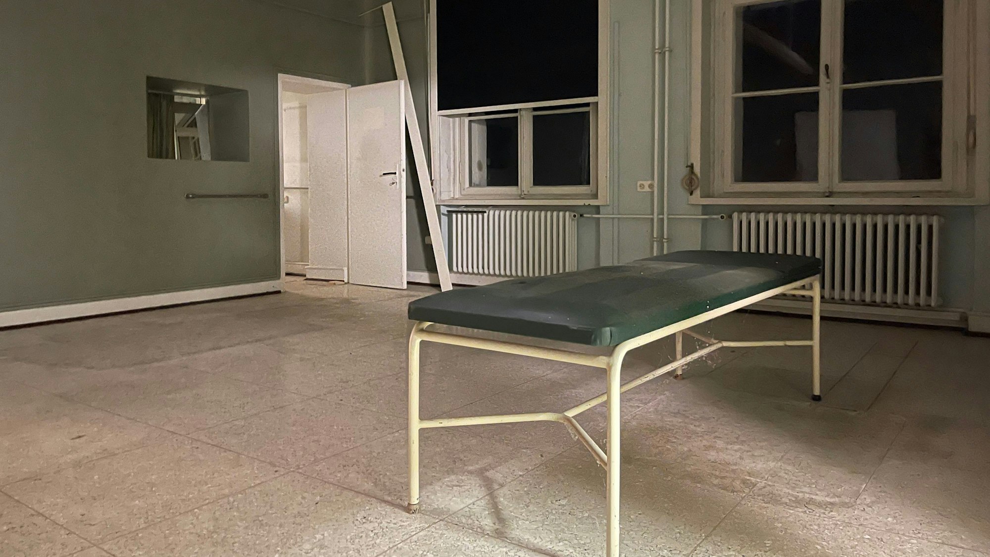 Eine Metallliege steht in einem Raum mit hohen Decken und alten Fesntern.