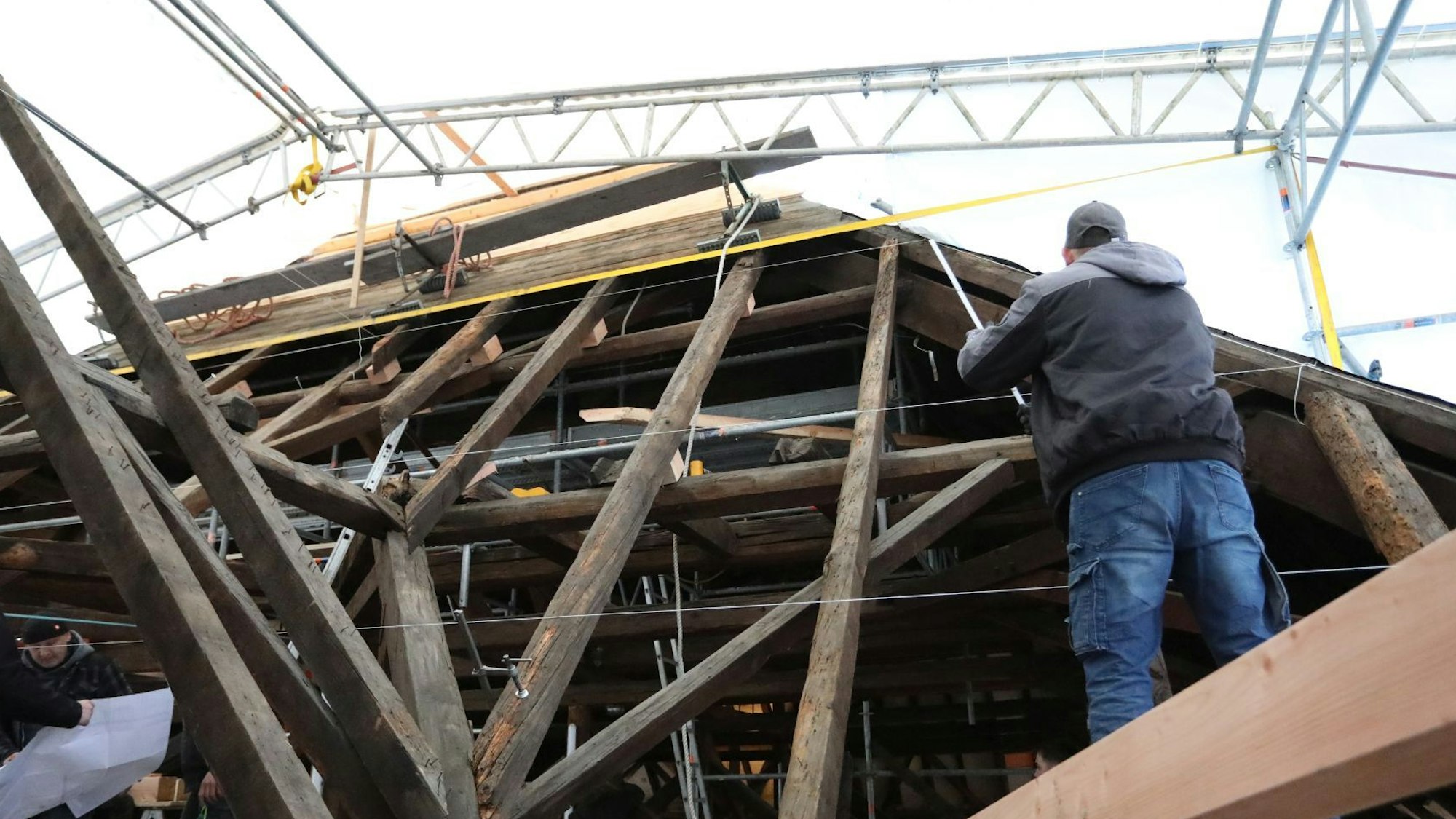 Neben den freiliegenden Holzbalken, die den Dachstuhl bilden, arbeitet ein Handwerker.
