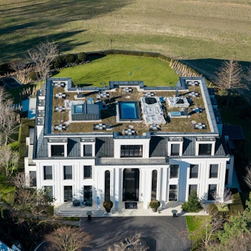 Eine Flugaufnahme zeigt eine umzäunte Villa mit einem weitläufigen Garten und ein paar Bäumen.