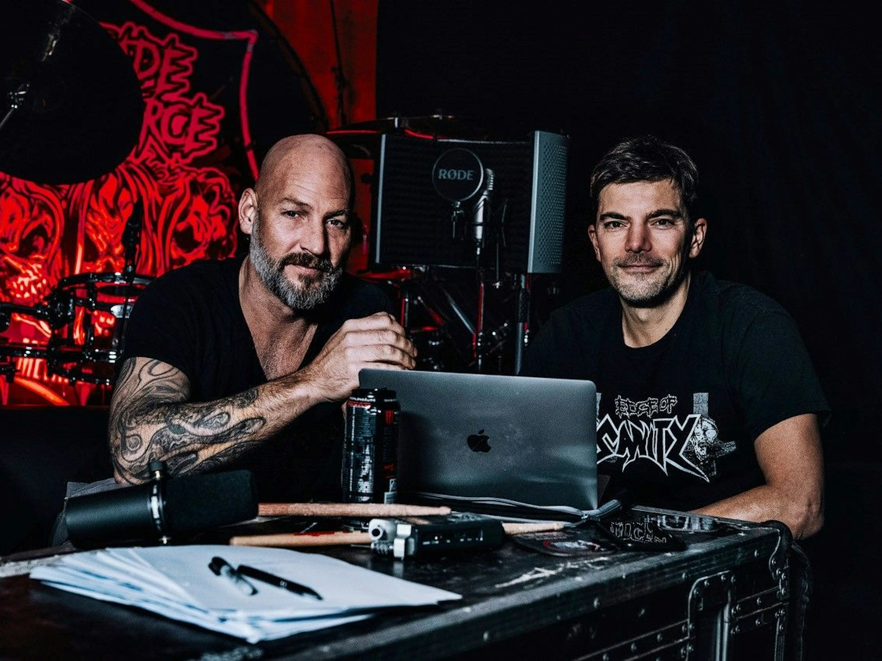 Zwei Männer sitzen an einem Laptop, die tragen schwarze Shirts.