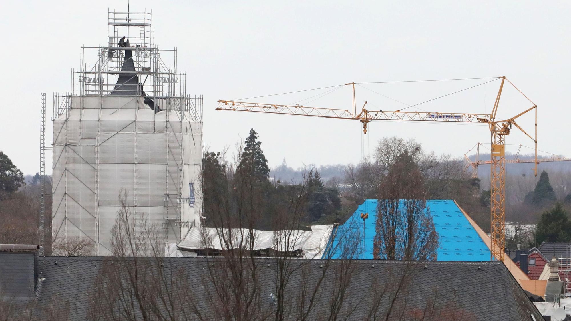 Der Turm einer Kirche ist eingerüstet und mit Planen verhangen, neben der Kirche steht ein gelber Baukran.