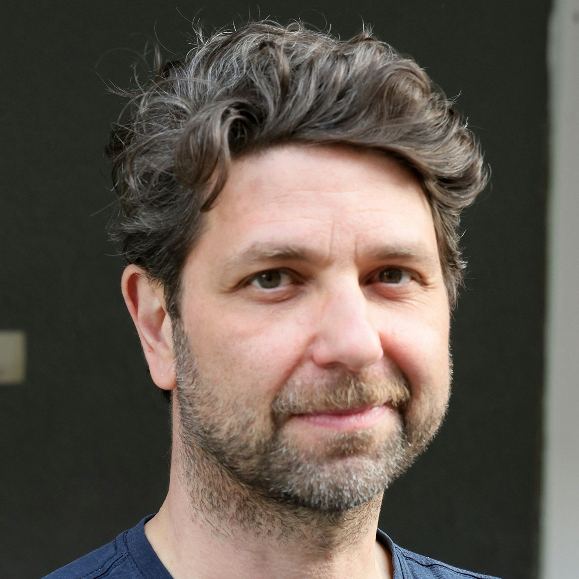 Ein Mann mit Bart und dunklen Haaren schaut in die Kamera