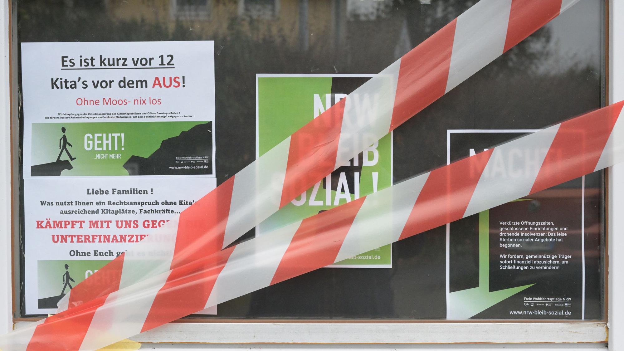 Auf dem Fenster einer Kita kleben Protestplakate und rot-weißes Absperrband.