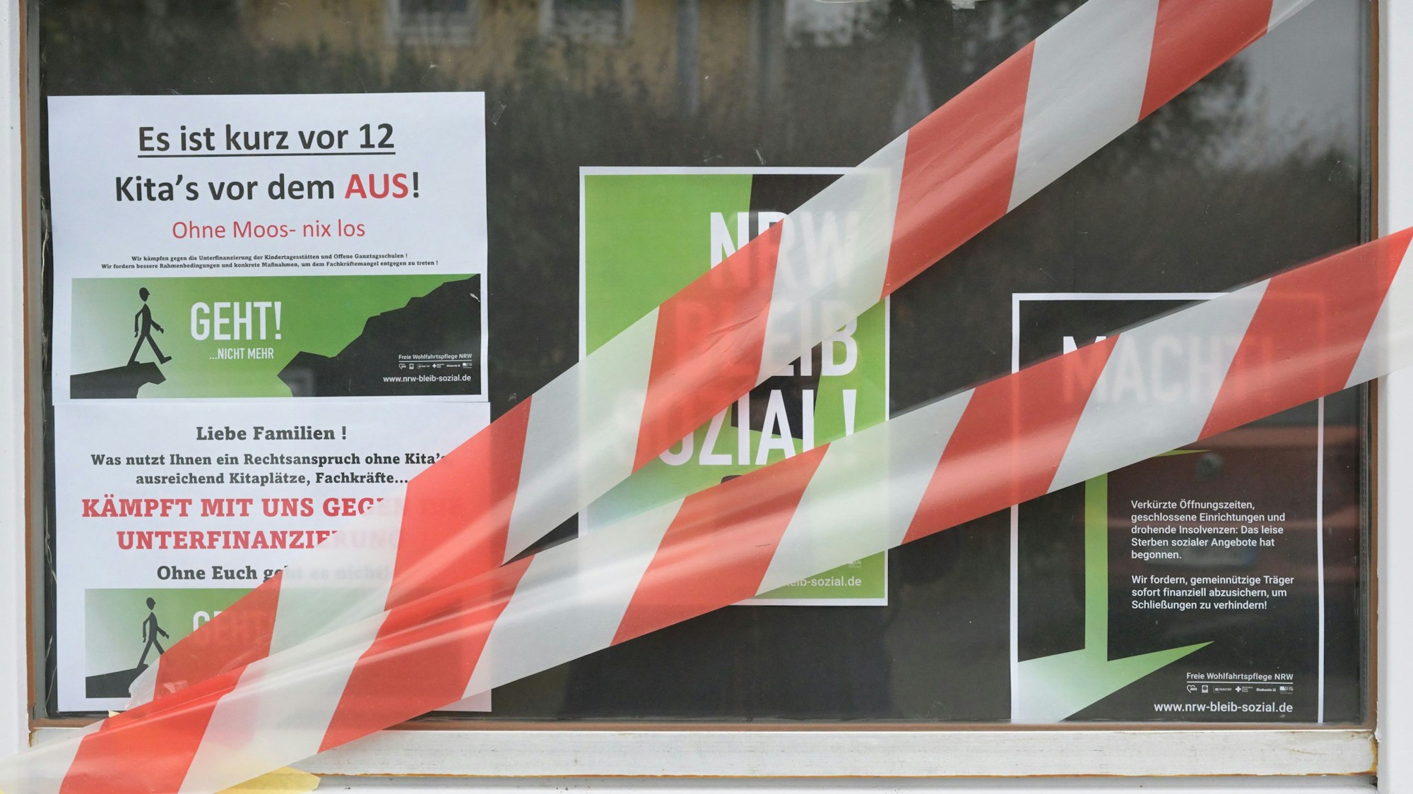 Auf dem Fenster einer Kita kleben Protestplakate und rot-weißes Absperrband.