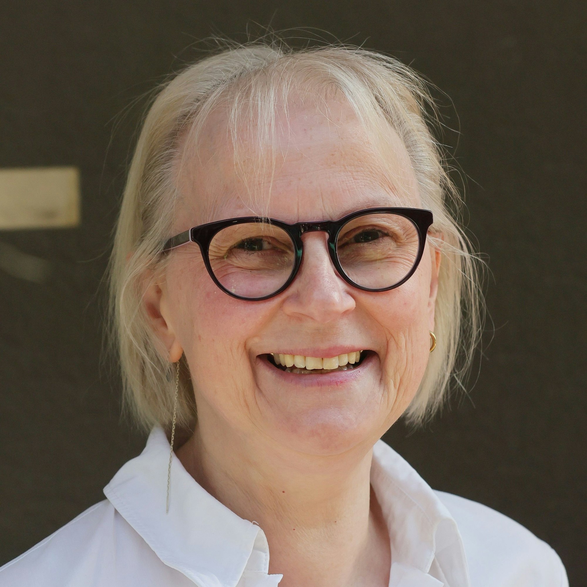 Eine Frau mit Brille lacht in die Kamera.