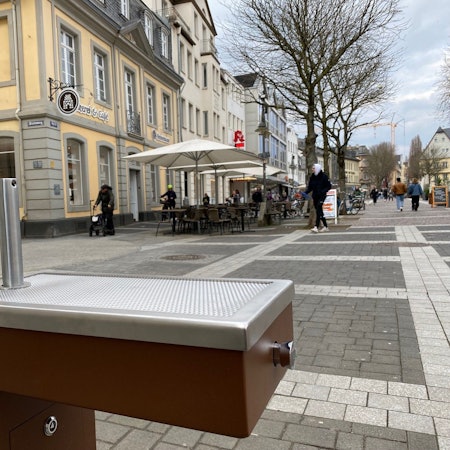Zu sehen ist einer der Trinkwasserbrunnen, im Hintergrund sieht man die Brühler Fußgängerzone.