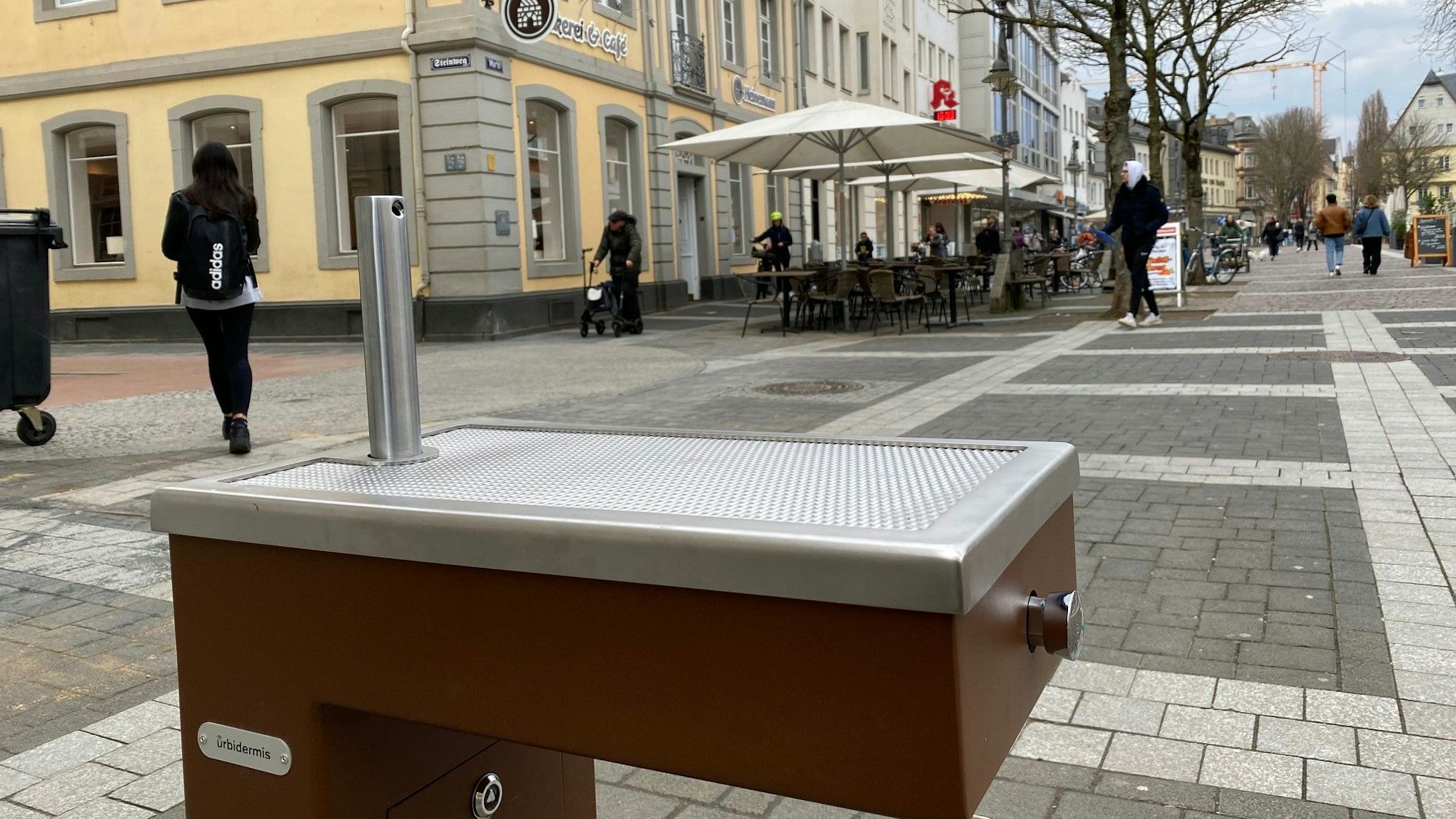 Zu sehen ist einer der Trinkwasserbrunnen, im Hintergrund sieht man die Brühler Fußgängerzone.