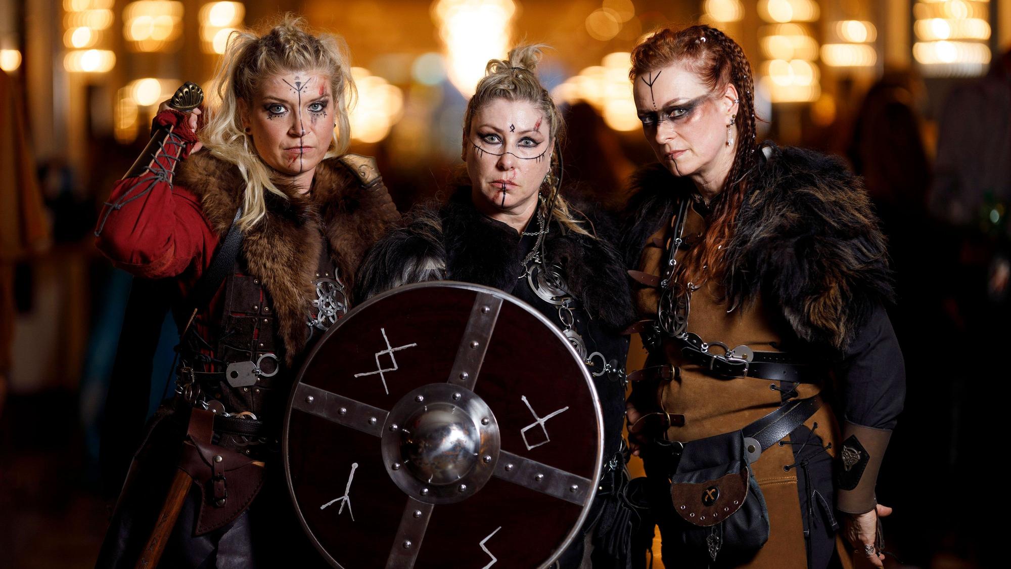 Drei Frauen sind als Wikingerfrauen aus der Serie „Vikings“ verkleidet. Sie tragen Fell, Lederkluften Schwerter und ein Rundschild, das mit Runen beschriftet ist.
