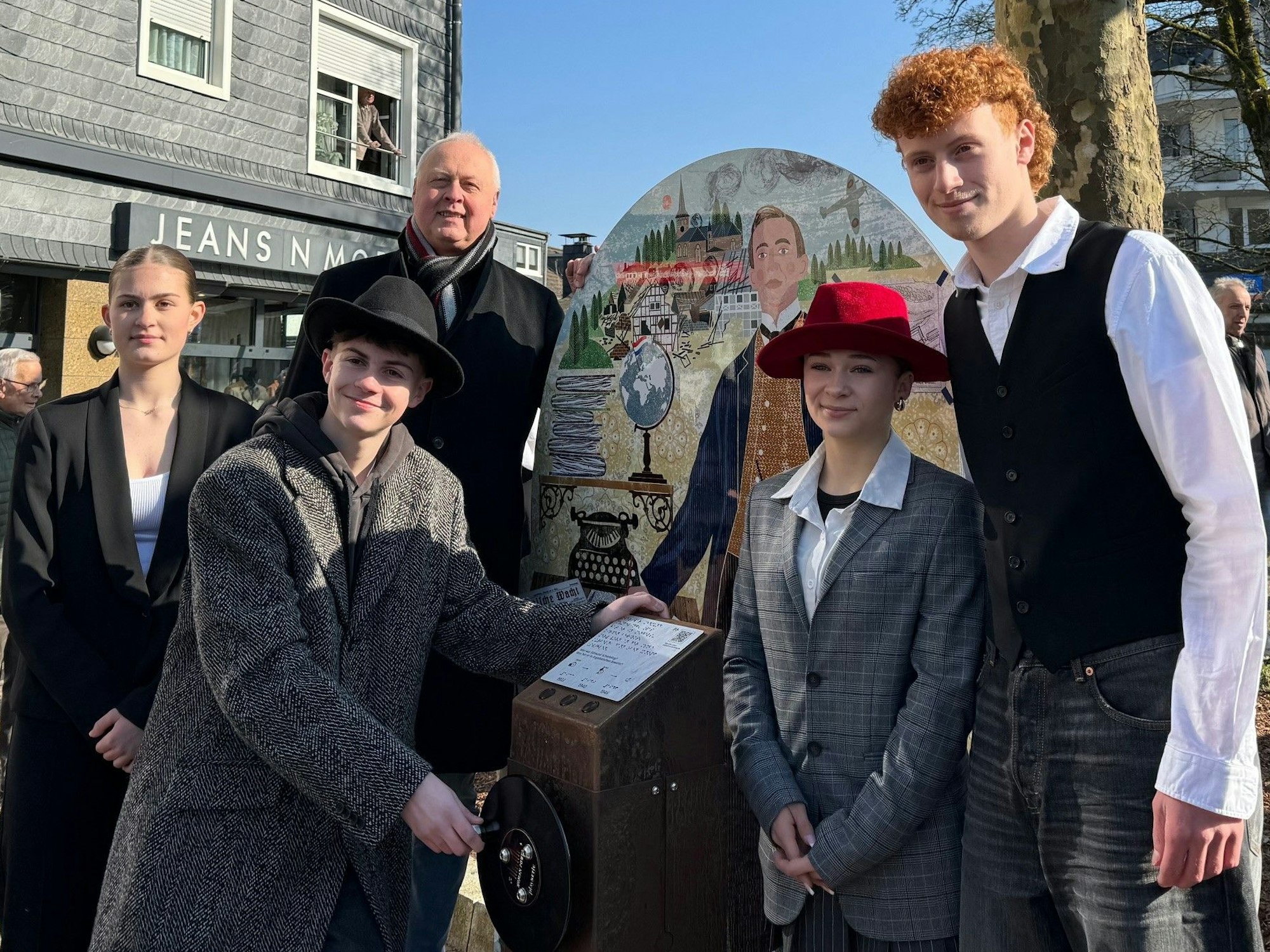 Fünf Menschen stehen zusammen, sie zeigen ein Schaubild und eine Audiostele mit Kurbel.