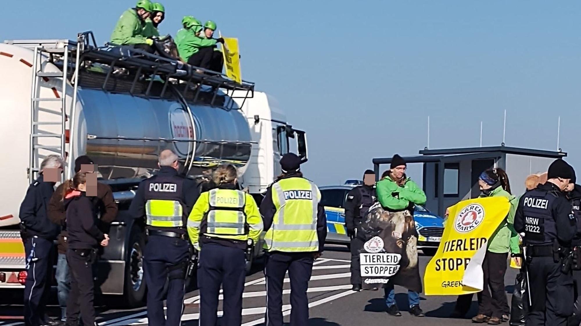 Auf dem Lkw sitzen fünf Greenpeace-Demonstranten, davor stehen weitere Protestler sowie mehrere Polizeibeamte.