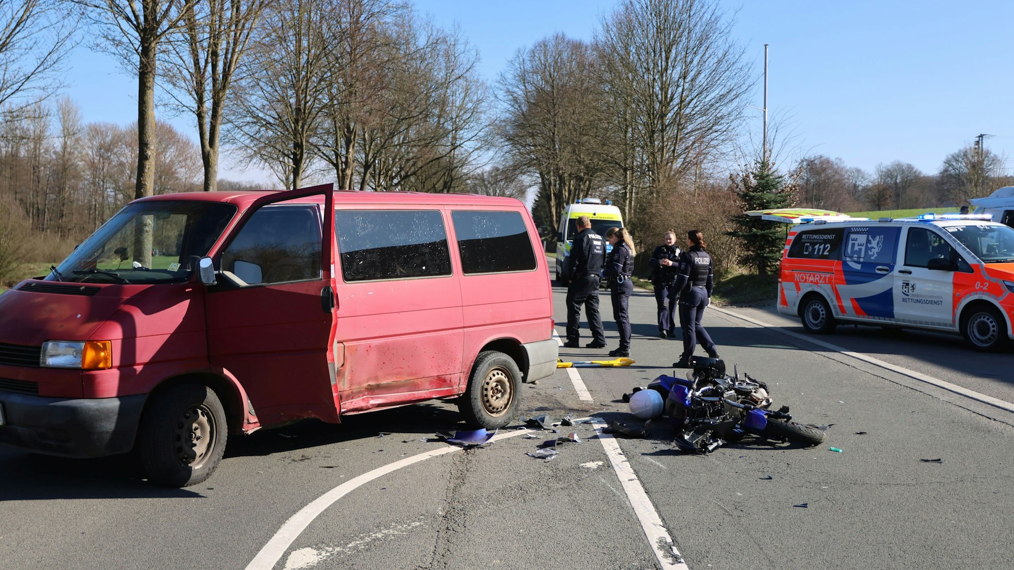 Ein Unfallfoto: Ein roter Transporter steht mit offener Türe auf der Straße. Ein Motorrad liegt komplett zerstört auf dem Biden. Im Hintergrund sind Einsatzfahrzeuge und mehrere Polizisten zu sehen.