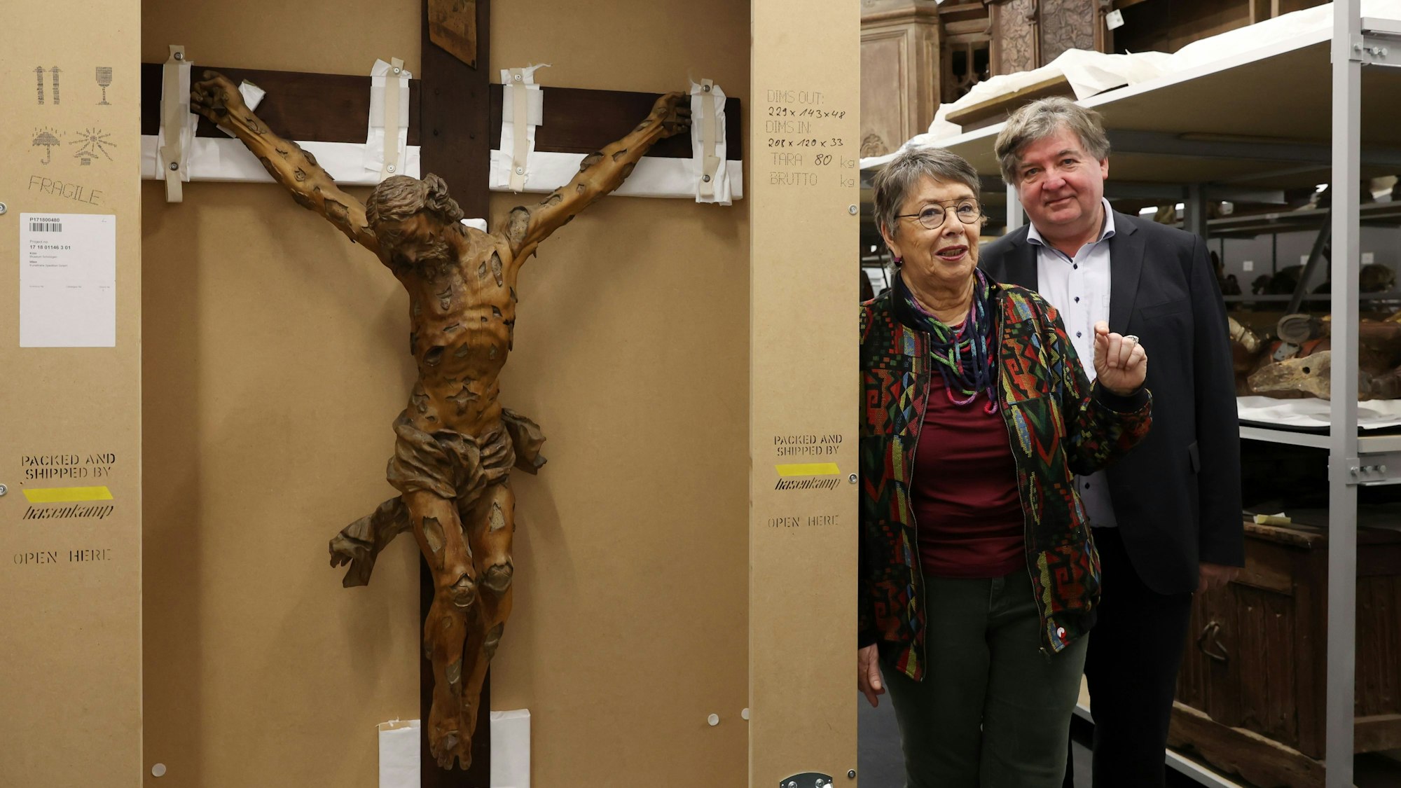 Ein Kruzifixus in Transportverpackung im Depot des Museum Schnütgen. Direktor Moritz Woelk (rechts) lässt das Kunstwerk eigens für die Sonderführungen von Dombaumeisterin a.D. Barbara Schock-Werner in die Ausstellungsräume des Museums bringen.
