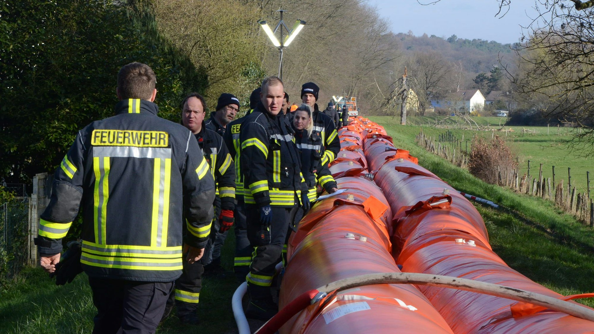 Feuerwehrleute neben den Schläuchen eines Hochwasserschutzsystems. Die Schläuche reichen ihnen bis zur Hüfte.