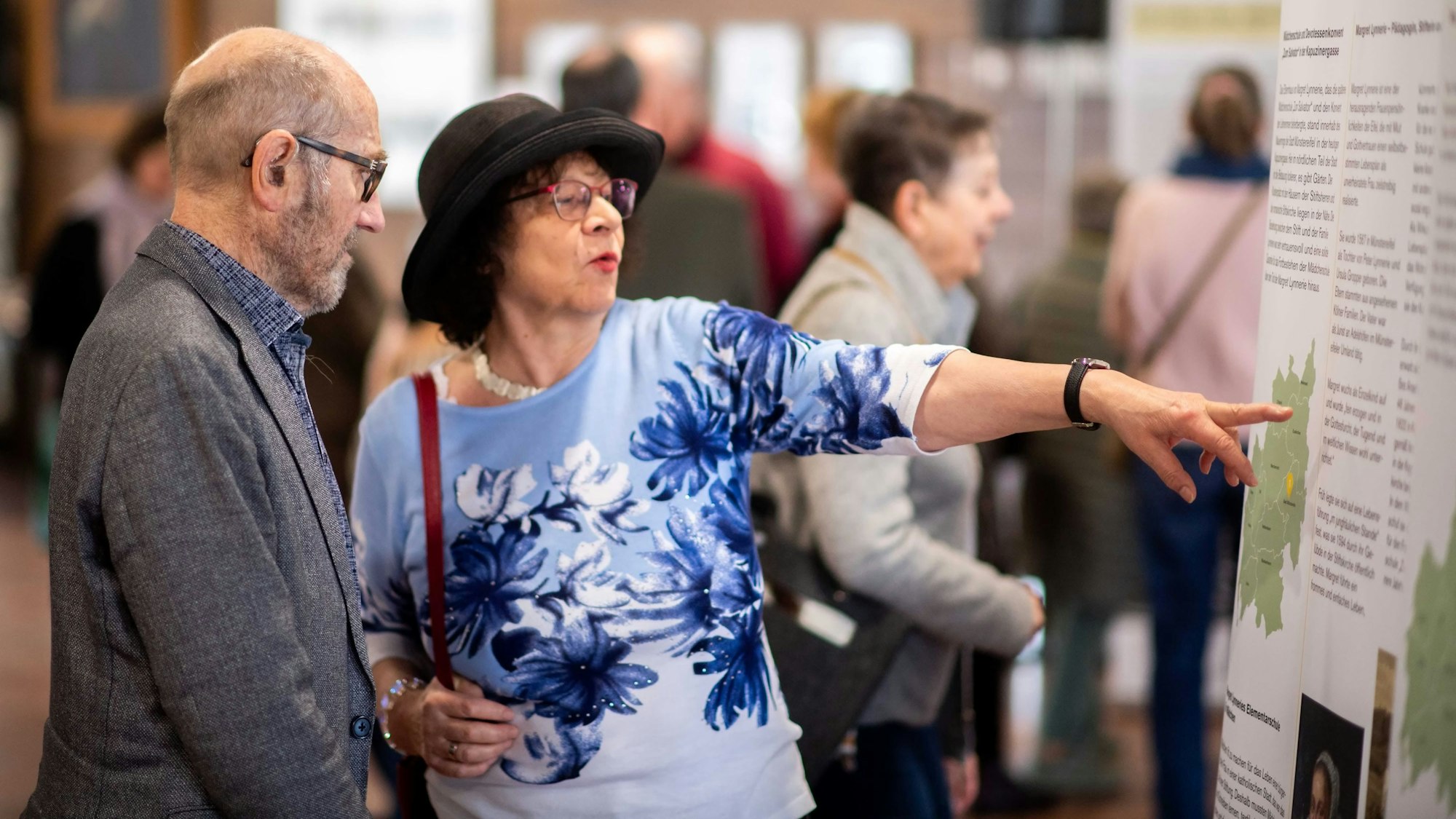 Eine Frau mit Hut zeigt ein Roll-up, das Teil der Ausstellung "Frauenorte" im Euskirchener Kreishaus ist.