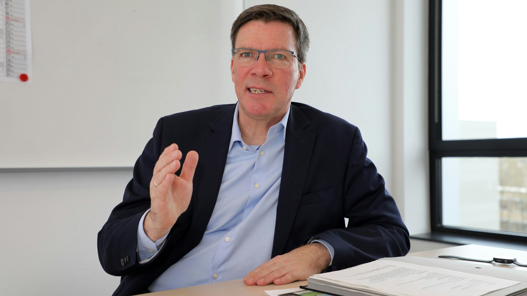 Landrat Stephan Santelmann sitzt an einem Tisch im Kreishaus am Rübezahlwald in Bergisch Gladbach und spricht.