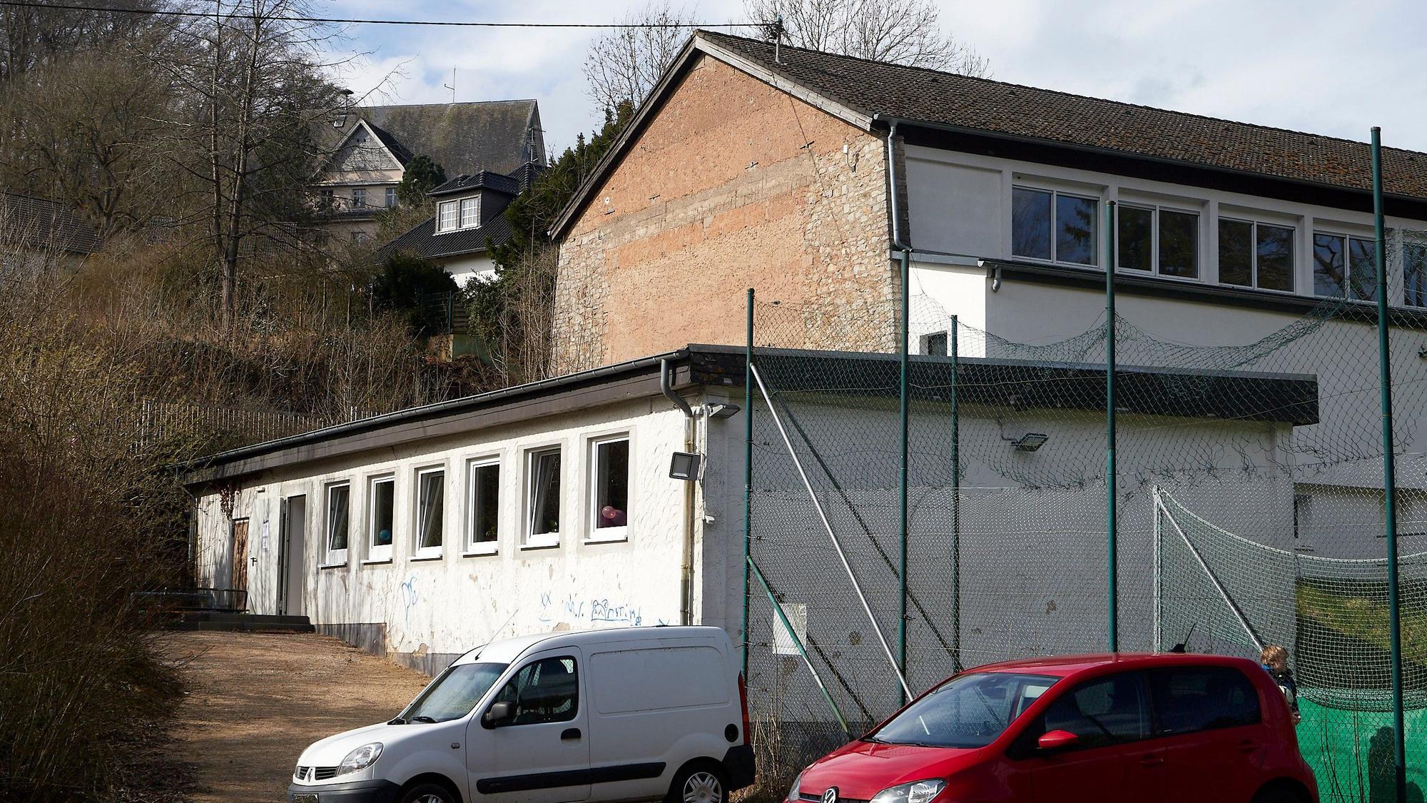 Ein rotes und ein weißes Auto parken vor dem Eingang zum Jugendraum in Blankenheim, der in dem weißen Gebäude ist.