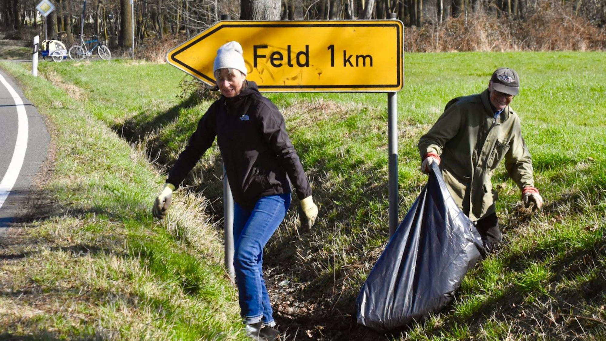 Frühjahrsputz der Kommunen im Rhein-Sieg-Kreis. In Much sammelte das Ehepaar Kurtenbach entlang der Straße: Eine Frau mit Mütze und ein Mann mit Kappe klettern in einem Graben entlang einer Straße, beide tragen Handschuhe. Er hält einen Müllsack in der Hand.