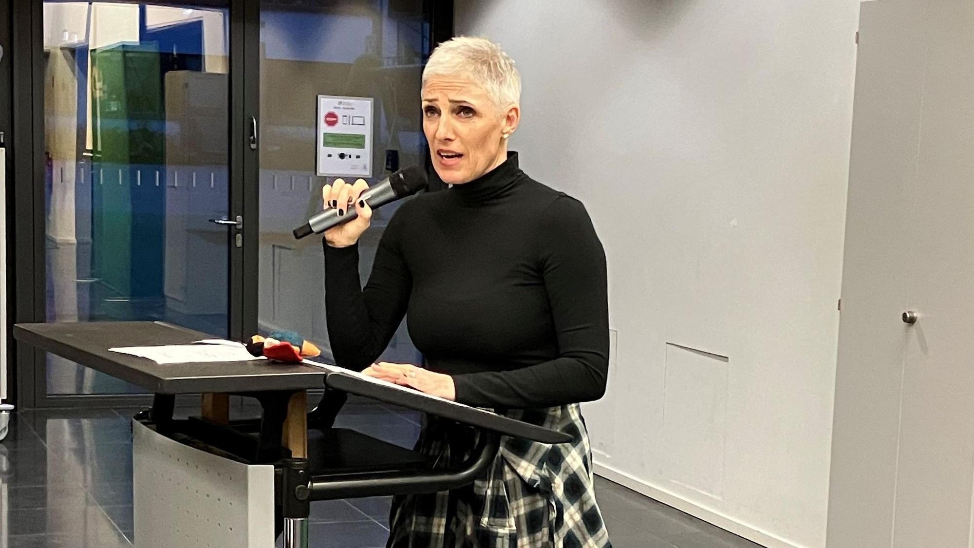 Bernadette Reinery-Hausmann bei einem Vortrag, mit Mikrofon in der Hand.