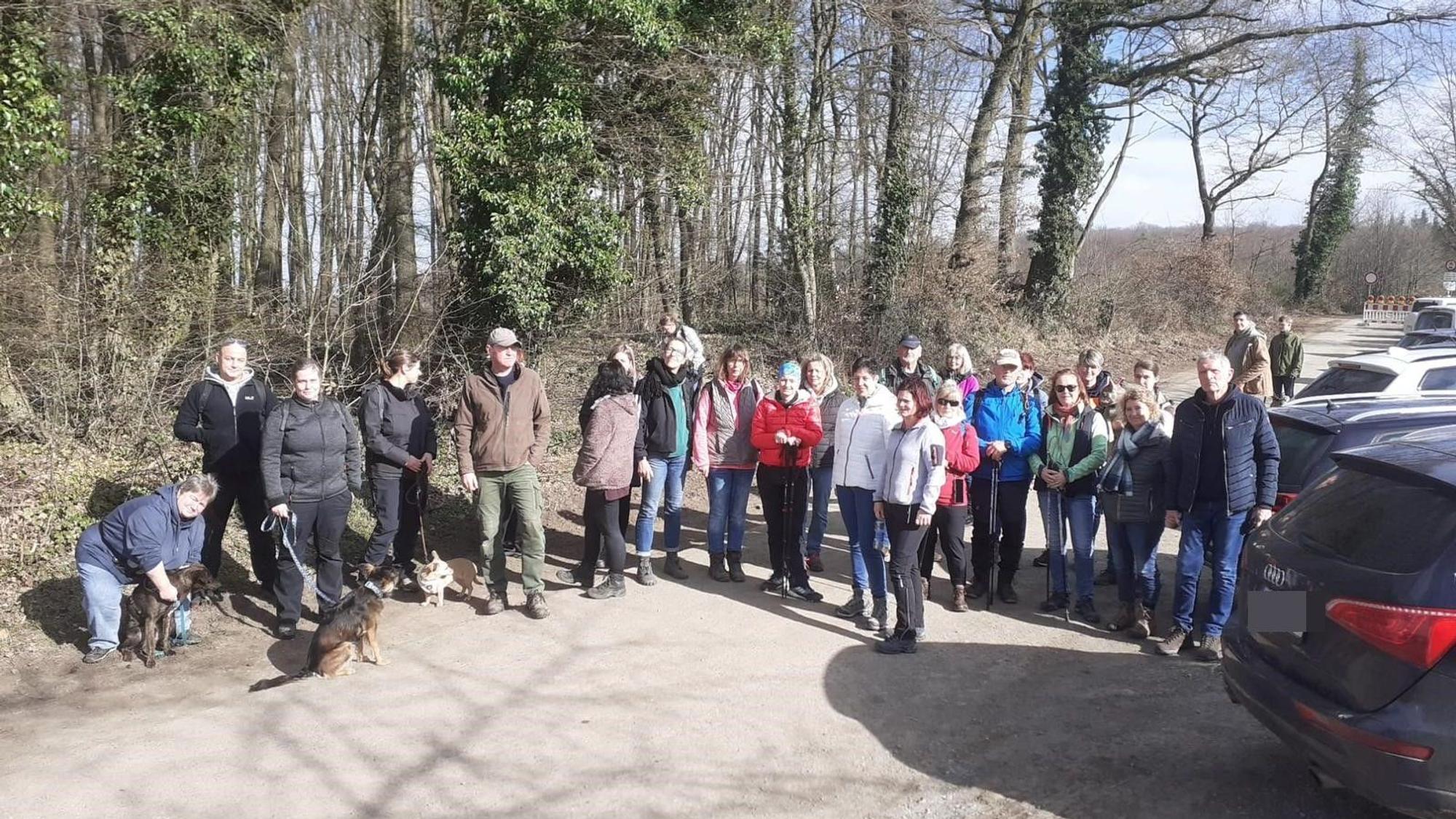 Menschen, zum Teil mit Hunden, stehen an einem Waldrand.
