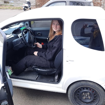 Eine Jugendliche sitzt auf dem Fahrersitz eines Micro-Cars, das Mini-Auto ist eine Alternative zum Mofa.