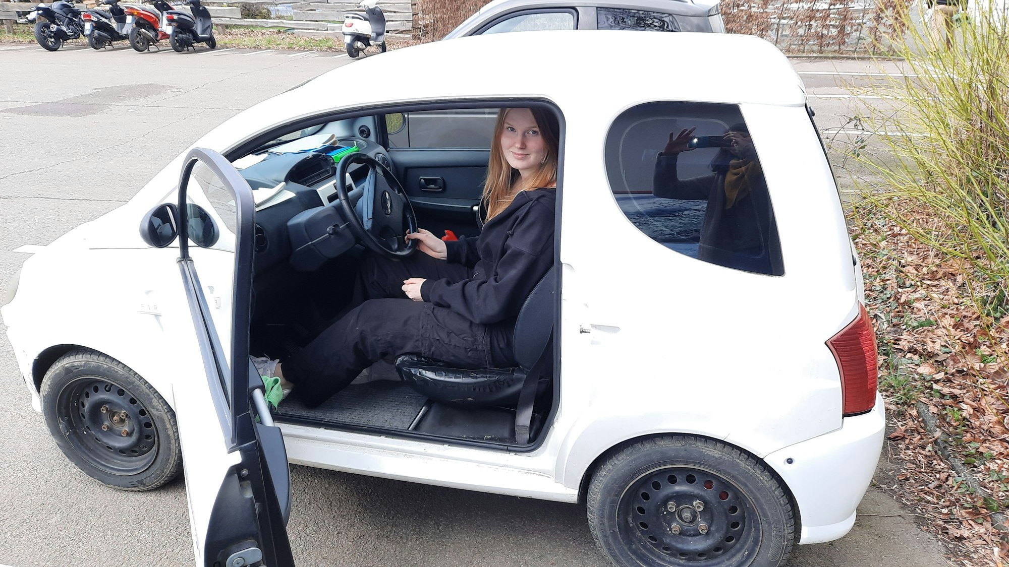 Eine Jugendliche sitzt auf dem Fahrersitz eines Micro-Cars, das Mini-Auto ist eine Alternative zum Mofa.