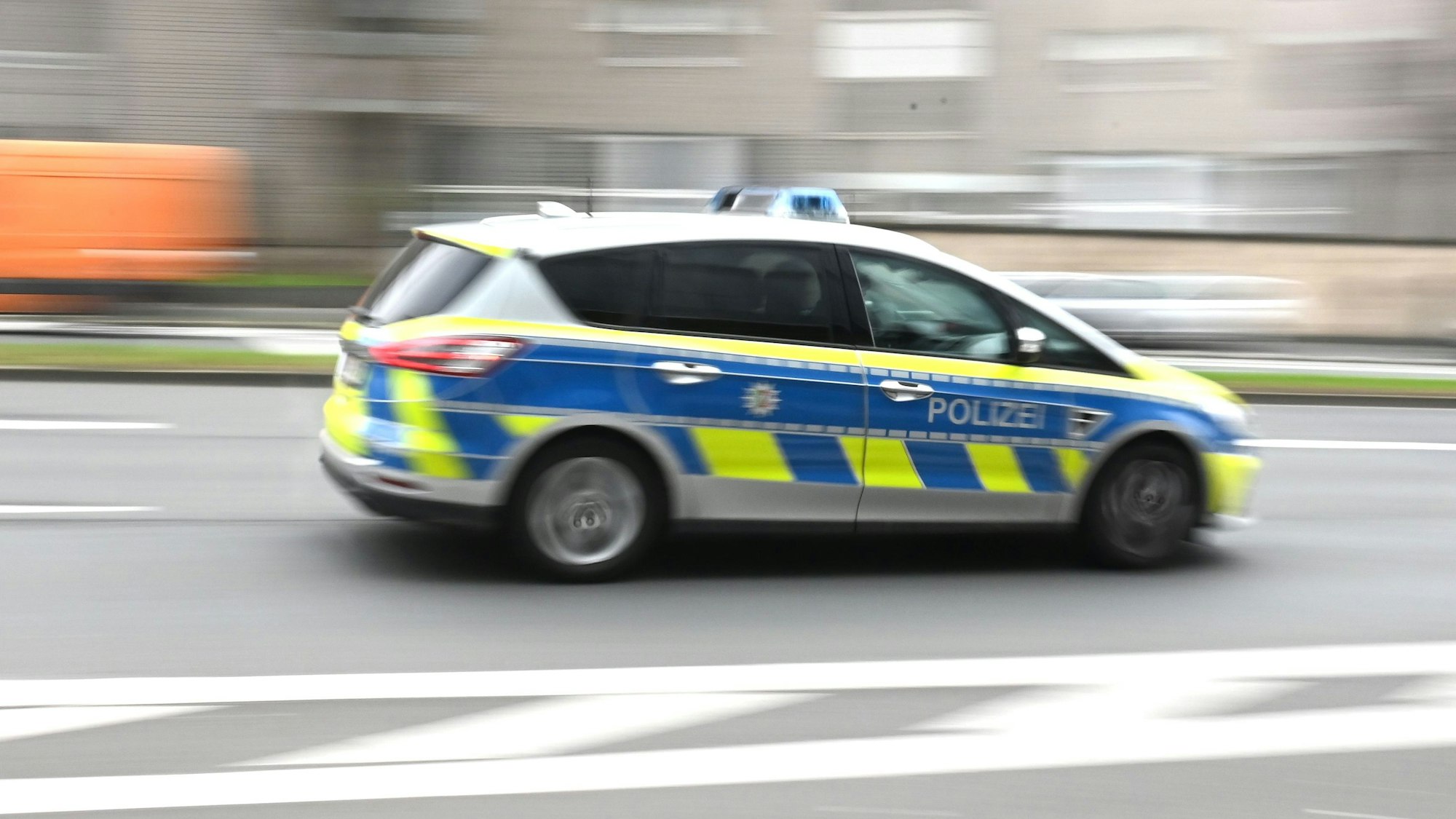 Zu sehen ist ein Polizeiwagen in der Seitenansicht, der durch die Kölner Innenstadt rast.