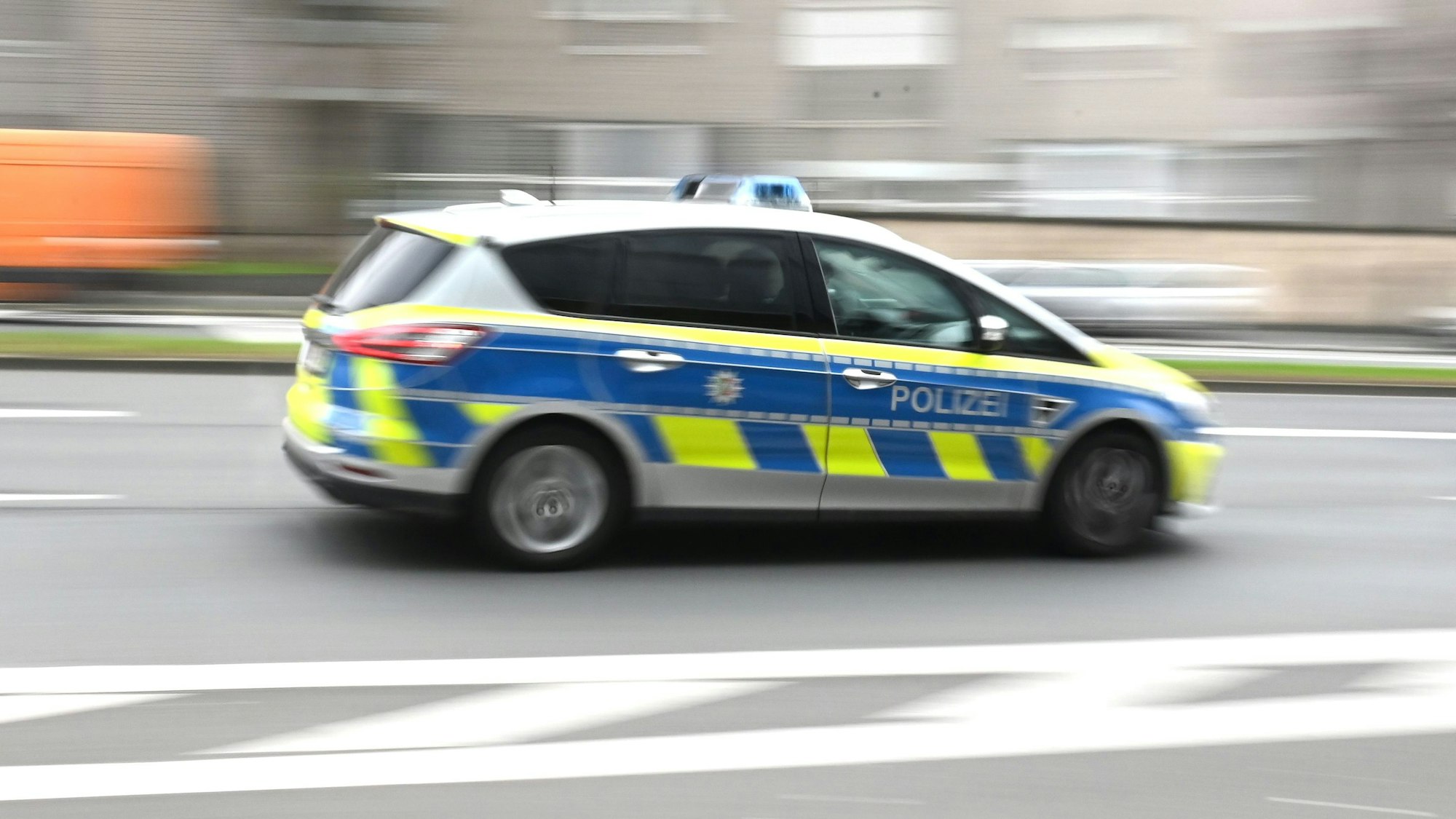 Zu sehen ist ein Einsatzfahrzeug der Kölner Polizei in der Seitenansicht, das durch die Innenstadt rast.