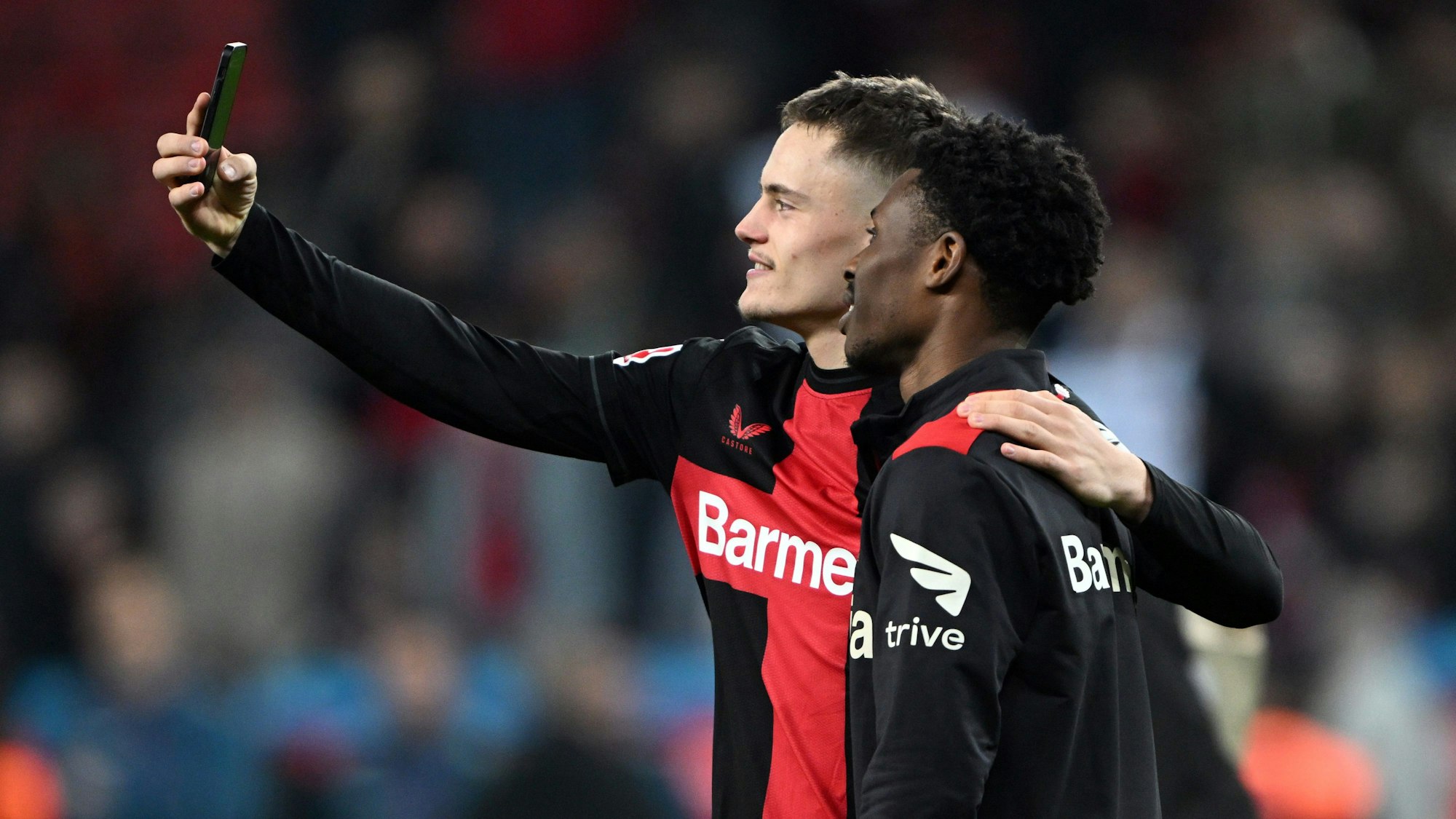 Leverkusens Florian Wirtz (l) und Nathan Tella machen ein Bild mit einem Handy.