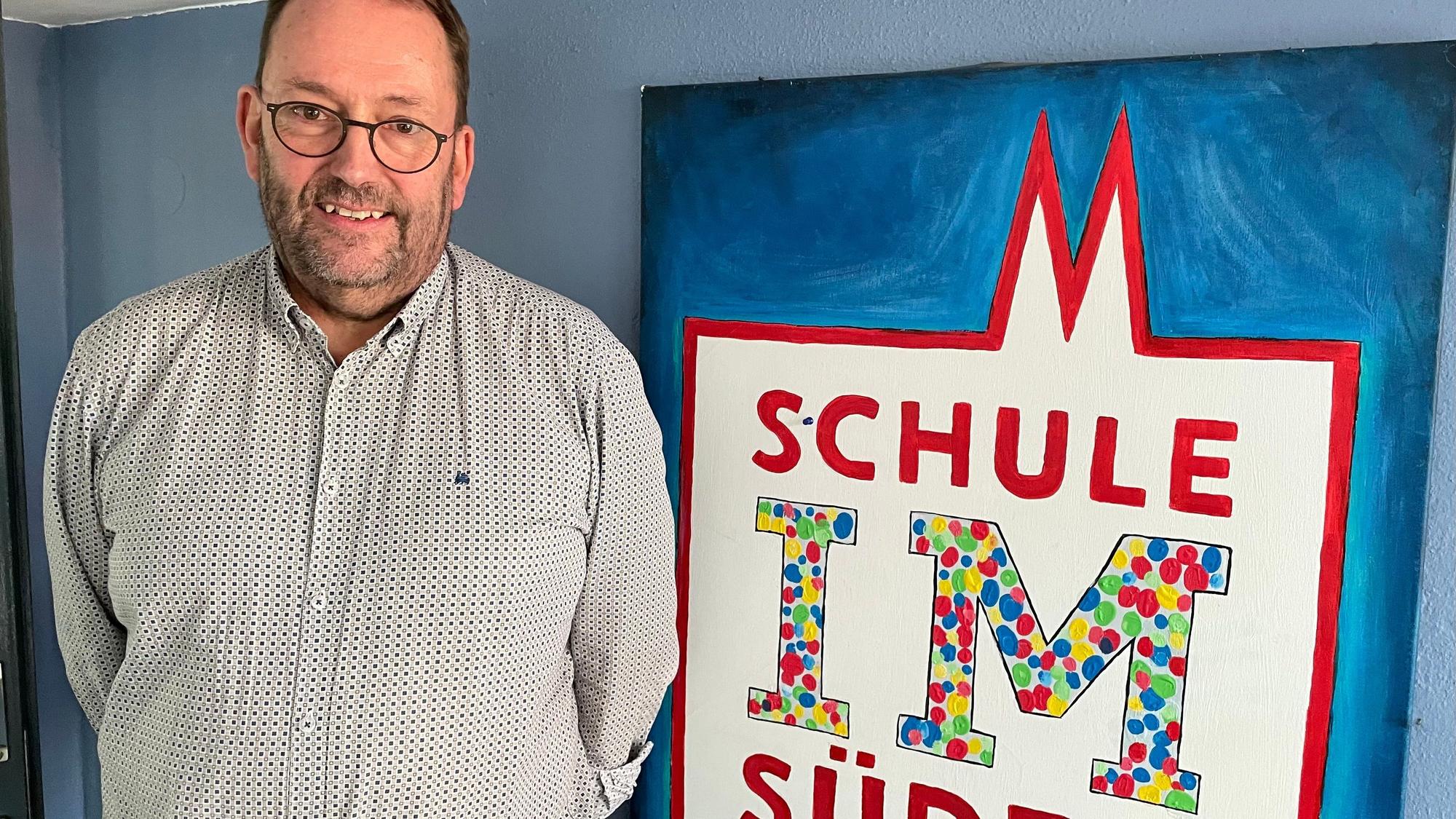 Ein Mann steht vor einem Plakat mit dem Namen der Schule IM Süden.