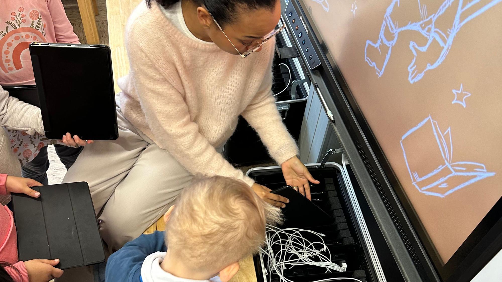 Zusammen mit den Kindern steckt Lehrerin Monika Nwuha-Junghof von der Hans-Christian-Andersen-Schule die I-Pads in die Ladestationen.