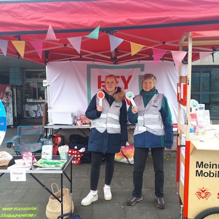 Unter der Plane eines Stands stehen zwei Frauen mit Smiley-Zeichen.