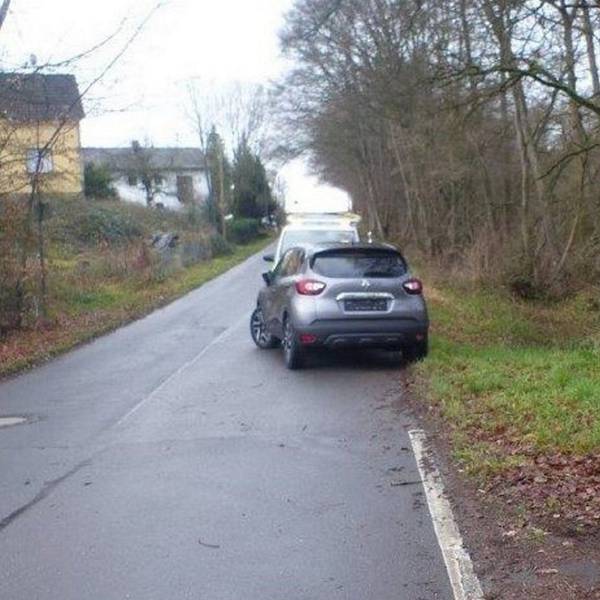 Ein Wagen steht an einer schmalen Straße halb auf der Fahrbahn.