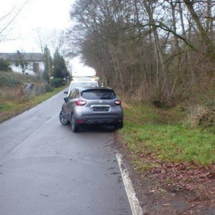Ein Wagen steht an einer schmalen Straße halb auf der Fahrbahn.