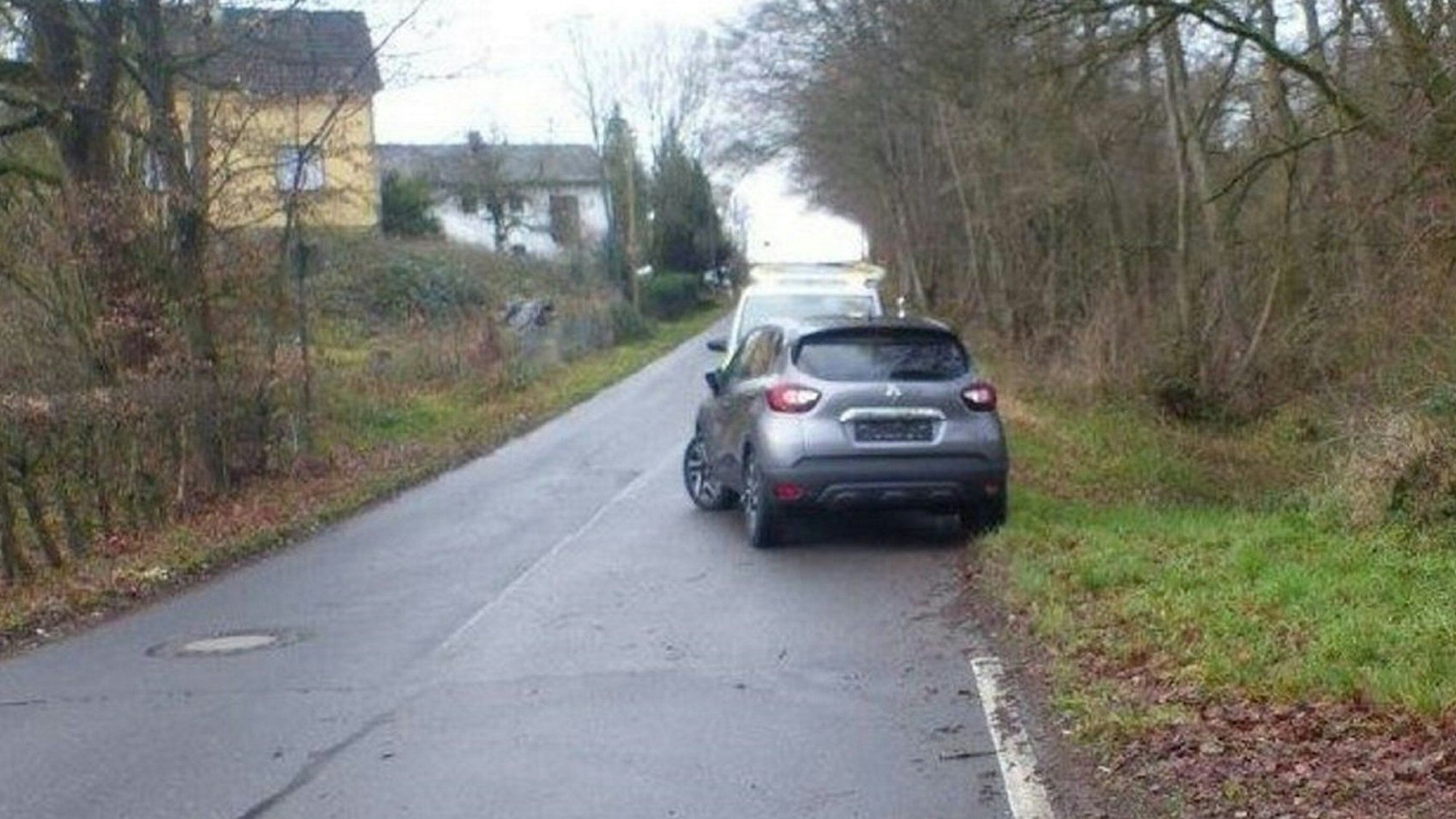 Ein Wagen steht an einer schmalen Straße halb auf der Fahrbahn.